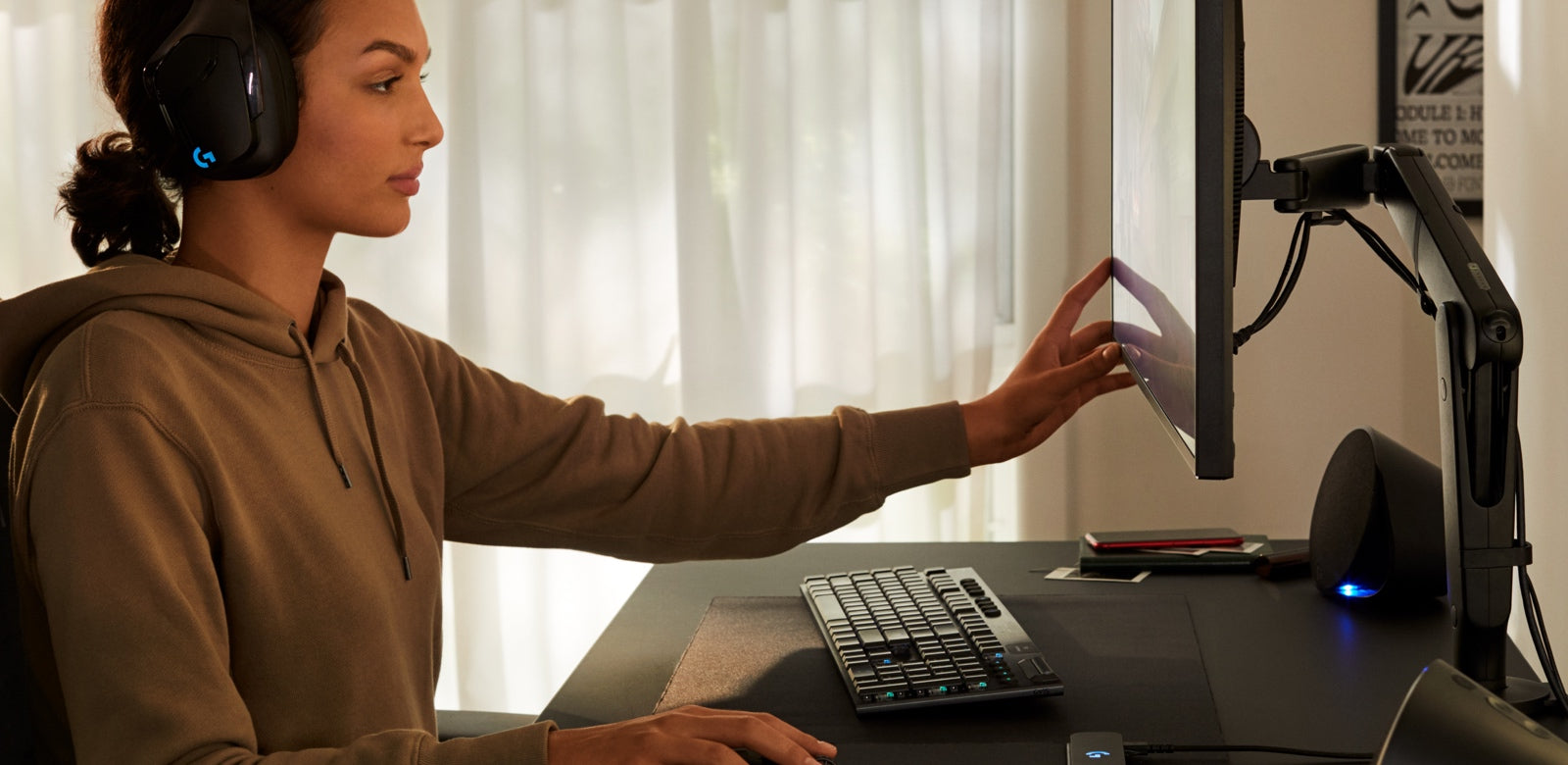 Una donna con una felpa regola un monitor collocato su un braccio porta monitor Ollin. Sullo sfondo si vedono delle tende bianche.