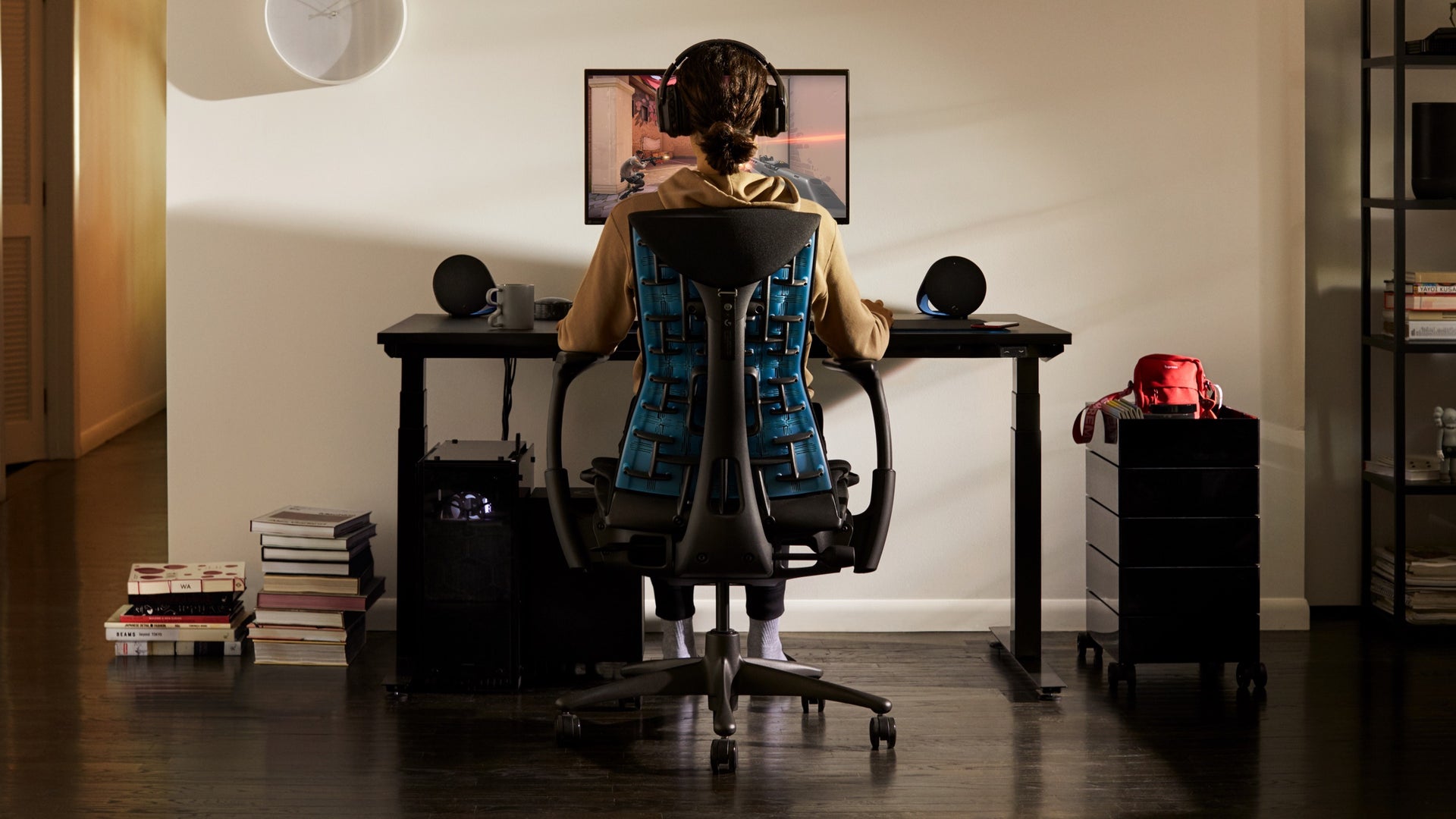 Una persona in una seduta per gaming Embody guarda un monitor posto su un braccio porta monitor Ollin, collocato su una scrivania per gaming in un ambiente domestico.